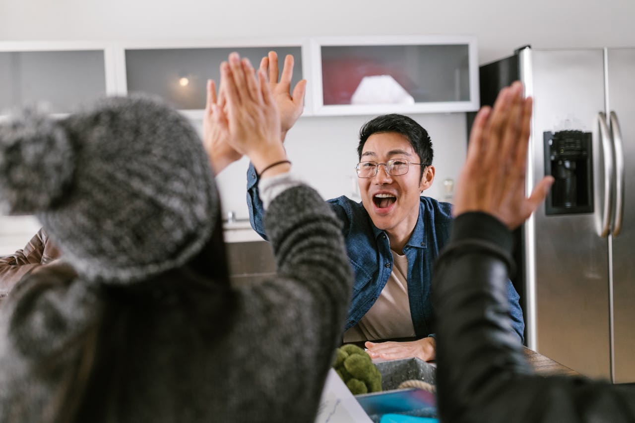 about-06 A diverse group of adults sharing a celebratory high five in a modern kitchen setting.