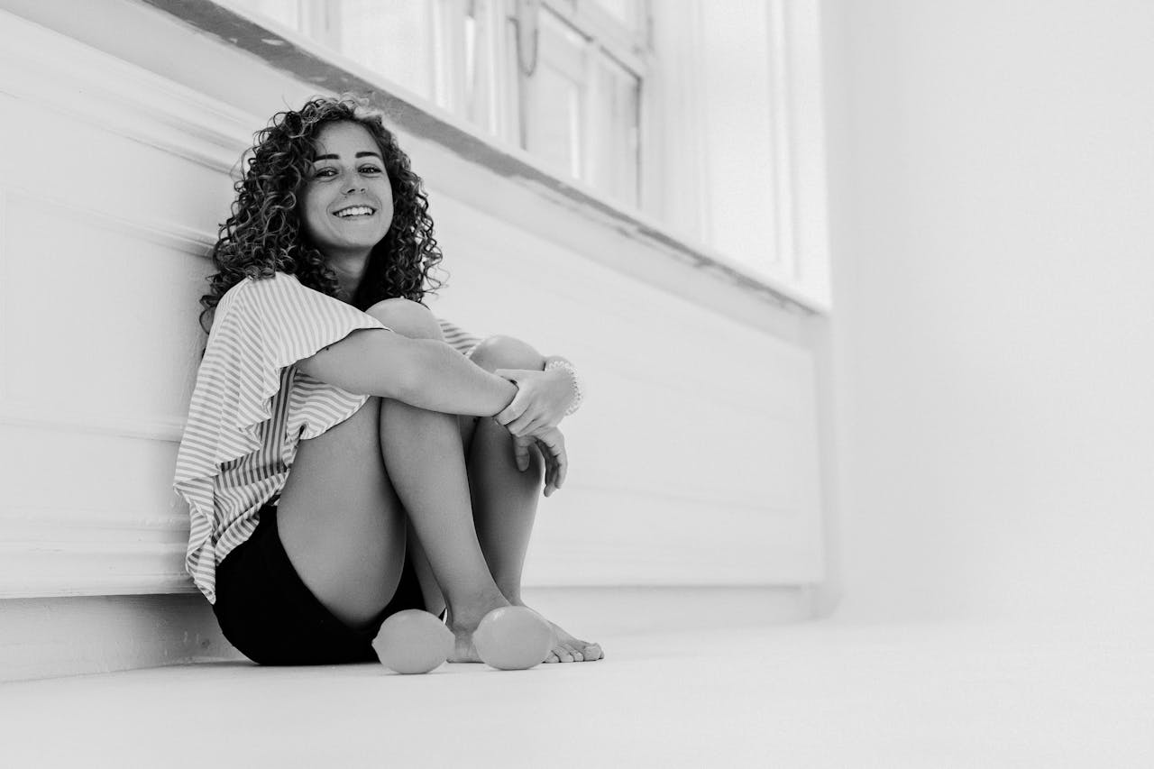 mission-02 Black and white photo of a woman sitting against a wall, smiling warmly.